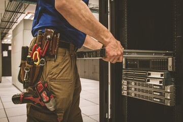 IT Engineer with a tool belt is pulling the server out out of the cabinet in the large data center