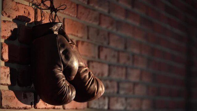 The shot shows a close up of a loft style brick wall with a nail nailed on it. A man then hangs up brown, boxing gloves. Hes a boxer and took them off after training