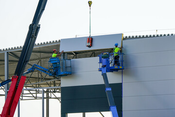 Naklejka premium Sandwich panels wall assembly using telescopic boom crane and two self propelled articulating lifts
