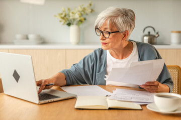 Middle aged senior woman sit with laptop and paper document, Pensive older mature lady reading paper bill pay online at home managing bank finances calculating taxes planning loan debt pension payment - Powered by Adobe
