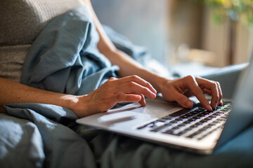 Close-up of hands typing on a laptop while relaxing in bed - obrazy, fototapety, plakaty