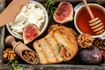 composition with delicious fig, toast, cream cheese, walnuts and honey in wooden box on a dark background. top view. place for text - obrazy, fototapety, plakaty