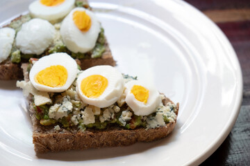 Sandwiches with avocado, blue cheese and boiled egg on white plate. Close up