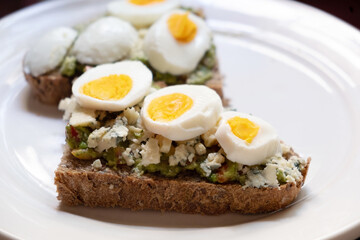 Sandwiches with avocado, blue cheese and boiled egg on white plate. Close up