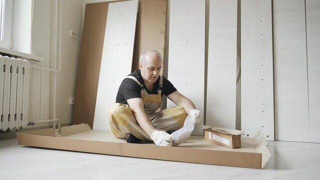 A male worker studies instructions before assembling furniture. Overall plan.