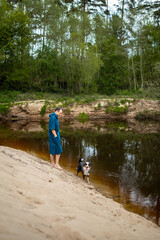 Fototapeta na wymiar Man in Teal Poncho Standing by the River, Dog Playing by the Riverside
