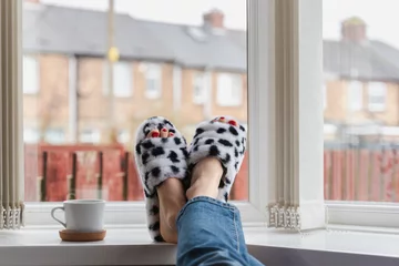 Poster Female legs wearing funny home slippers relaxing near the window © Leart