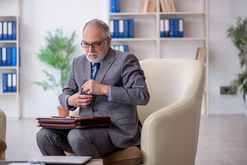 Old male employee sitting on arm-chair