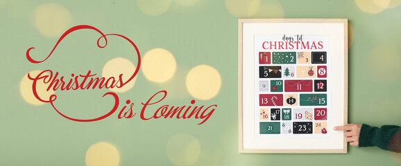 Female hand with Christmas advent calendar and text CHRISTMAS IS COMING on green background