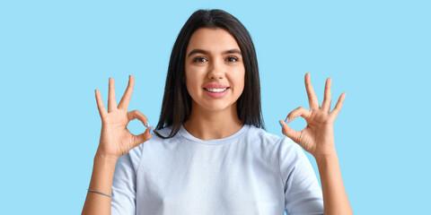 Smiling young woman showing OK on light blue background