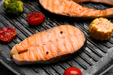 Tasty grilled salmon steaks and vegetables in frying pan, closeup