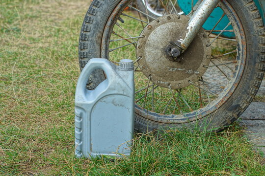 one  used empty flammable plastic canister with a gray machine oil with a handle on a green grass near a motorcycle wheel   on the street
