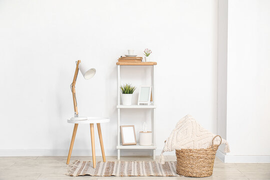 Desk lamp on small table and shelving unit with decor near white wall