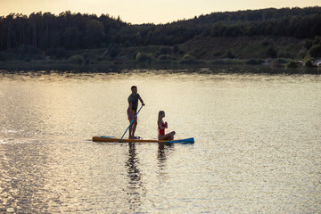 Woman meditating on supboard early morning with man paddling.