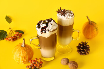Glass cups of tasty pumpkin latte with star anise, walnuts and viburnum on yellow background