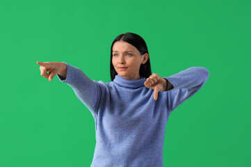 Young woman with dislike pointing at something on green background