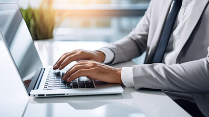 Businessman working on laptop. Grey suit and sun coming into office. Close up