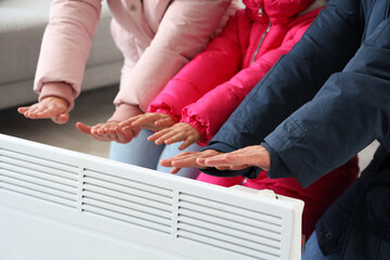 Frozen family in winter clothes warming near radiator at home, closeup