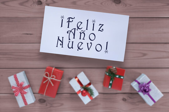 Happy New Year card : Feliz Ano Nuevo lettering in spanish. Greeting card with Inscription, gifts on wooden background. Top view, flat lay. Winter holidays in Spain. Preparing for Christmas.