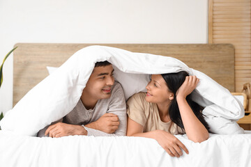 Young couple lying under blanket in bedroom