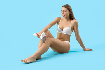 Beautiful young woman epilating her legs with modern photoepilator on blue background