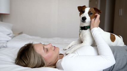 Dog friendly hotel. A girl and a dog sleep in a white bed at home. Happy mixed breed dog in a...
