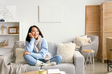 Foto op Canvas Young Asian woman sitting on sofa at home © Pixel-Shot