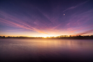 Sunrise at the quarry pond in Illingen. The sun's rays make the clouds glow while the stars still...