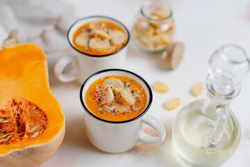 Roasted butternut squash soup with cream and pumpkin seeds on two white mugs.