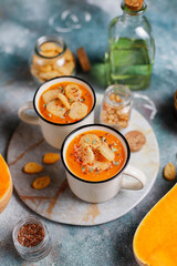 Roasted butternut squash soup with cream and pumpkin seeds on two white mugs.