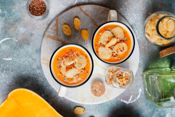 Roasted butternut squash soup with cream and pumpkin seeds on two white mugs.