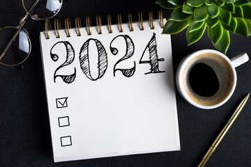 2024 New year resolutions on desk. 2024 goals list with notebook, coffee cup, plant on black table....
