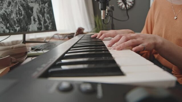 Close up shot of hands of female musician playing synthesizer at home recording studio