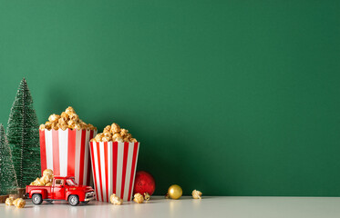 Spice up your winter holidays with popcorn delivery theme. Side view presents table featuring festive car, striped popcorn buckets, baubles, petite fir, green wall backdrop, allowing for movie promo