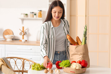 Young Asian woman unpacking fresh products from market at table in kitchen - Powered by Adobe