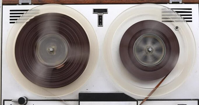Old reel-to-reel tape recorder rewinds magnetic tape, vintage music player close-up