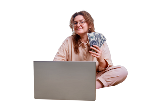 Happy woman holds money in dollars sitting on a home bed, isolated on a white background. Woman with a computer working remotely during isolation due to quarantine