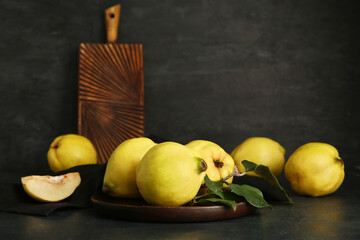 Plate with sweet ripe quinces and leaves on black background