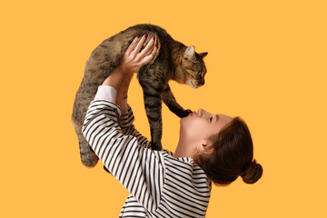 Pretty young woman kissing cute tabby cat on orange background - obrazy, fototapety, plakaty