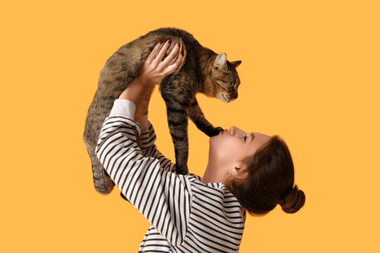 Pretty young woman kissing cute tabby cat on orange background