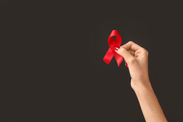 Female hand with red ribbon on black background. World AIDS Day concept