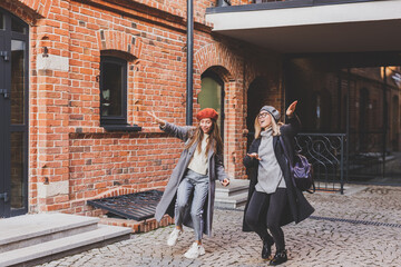 Millennial young women having fun and dance on city street. Female funny friends enjoying autumn day around the city.