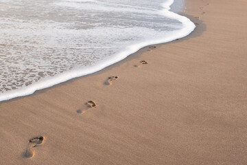 The wave washes away footprints in the sand - obrazy, fototapety, plakaty