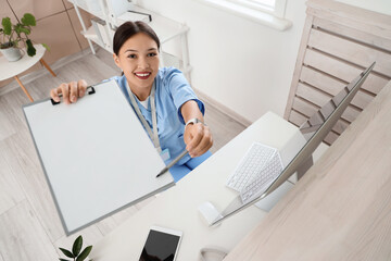Female Asian medical intern with clipboard at reception in clinic
