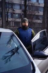 Bearded man wearing body armor near his car