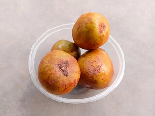 pile of ripe sapodilla fruit in a bowl on a gray background. fresh and healthy fruit.