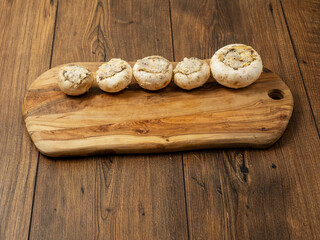 Stuffed mushrooms cups on a wooden board and table. High quality product with breadcrumbs, cheese and herbs ready for oven cooking.