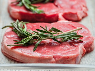 Juicy uncooked lamb leg steak with green fresh rosemary on plastic tray. Uncooked high quality meat product with rich taste and vivid color.