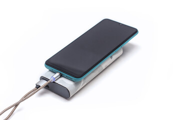 Modern smartphone is charged using a portable charger via a cable. Power bank in a camouflage case isolated on a white background. External battery for gadgets.