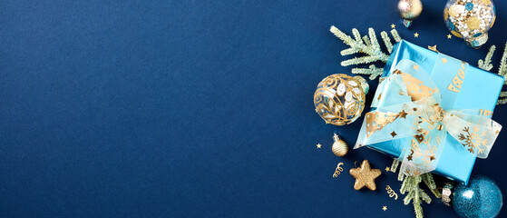 Christmas gift box with fir branches, gold Xmas ball ornaments, decorations, confetti on dark blue...